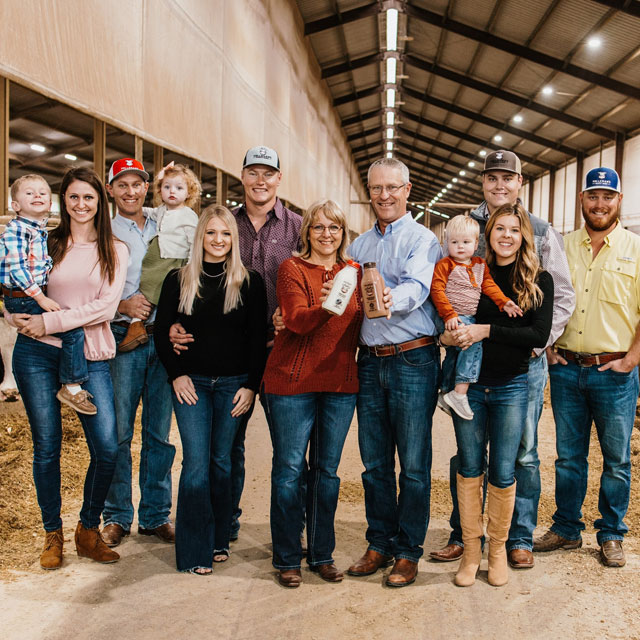 A Family of dairy farmers poses for a group photo, and the people range in age from toddler to elder.